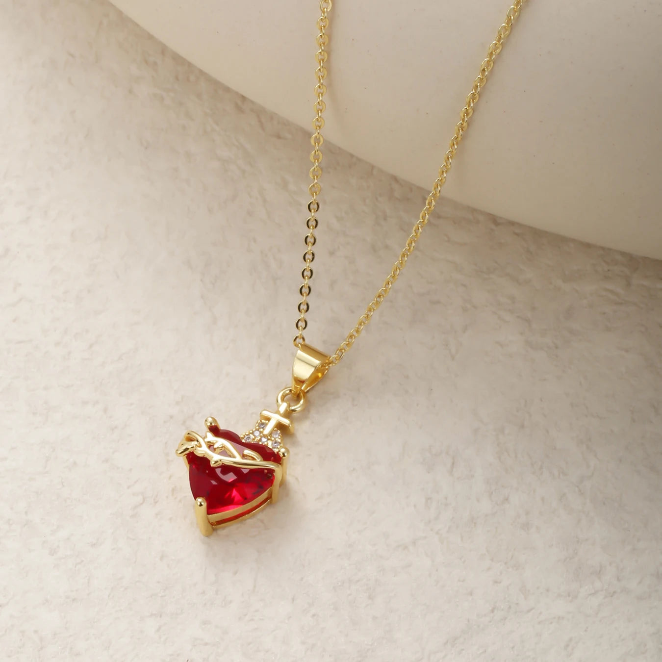 Gold necklace with a red heart pendant on a light gray background