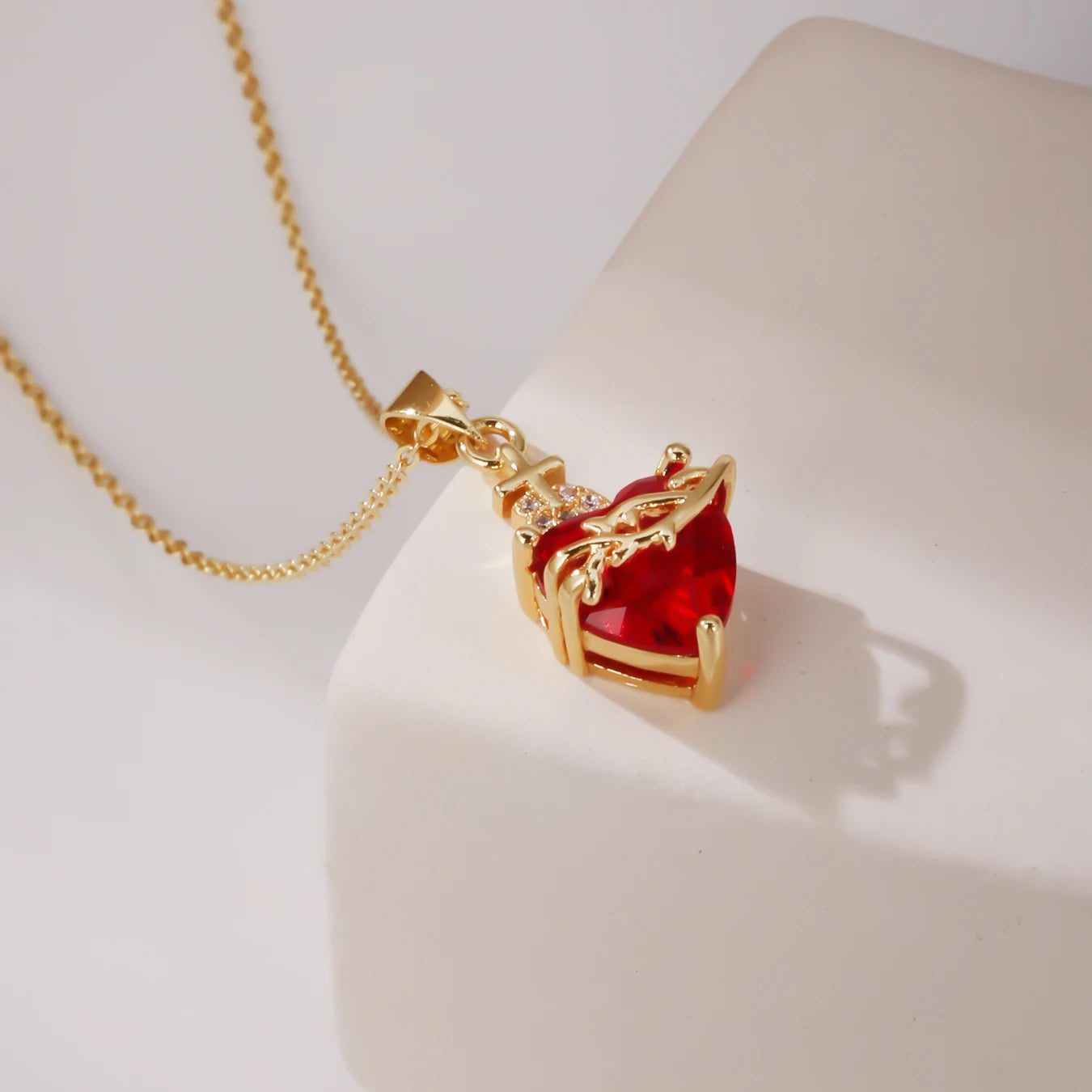 Gold necklace with a red heart-shaped pendant on a white surface