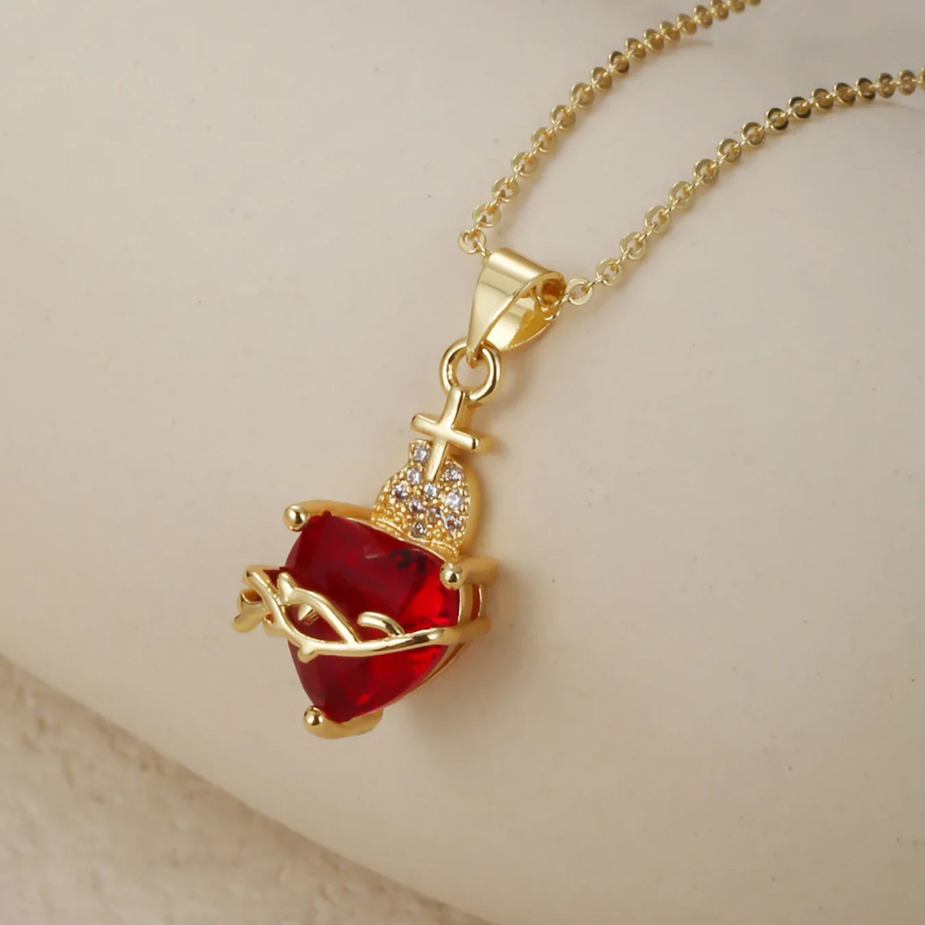 Gold necklace with a red gemstone pendant on a beige background