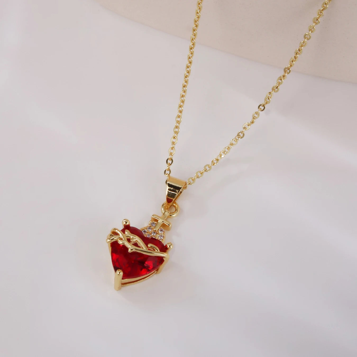 Gold necklace with a red heart-shaped pendant on a white background