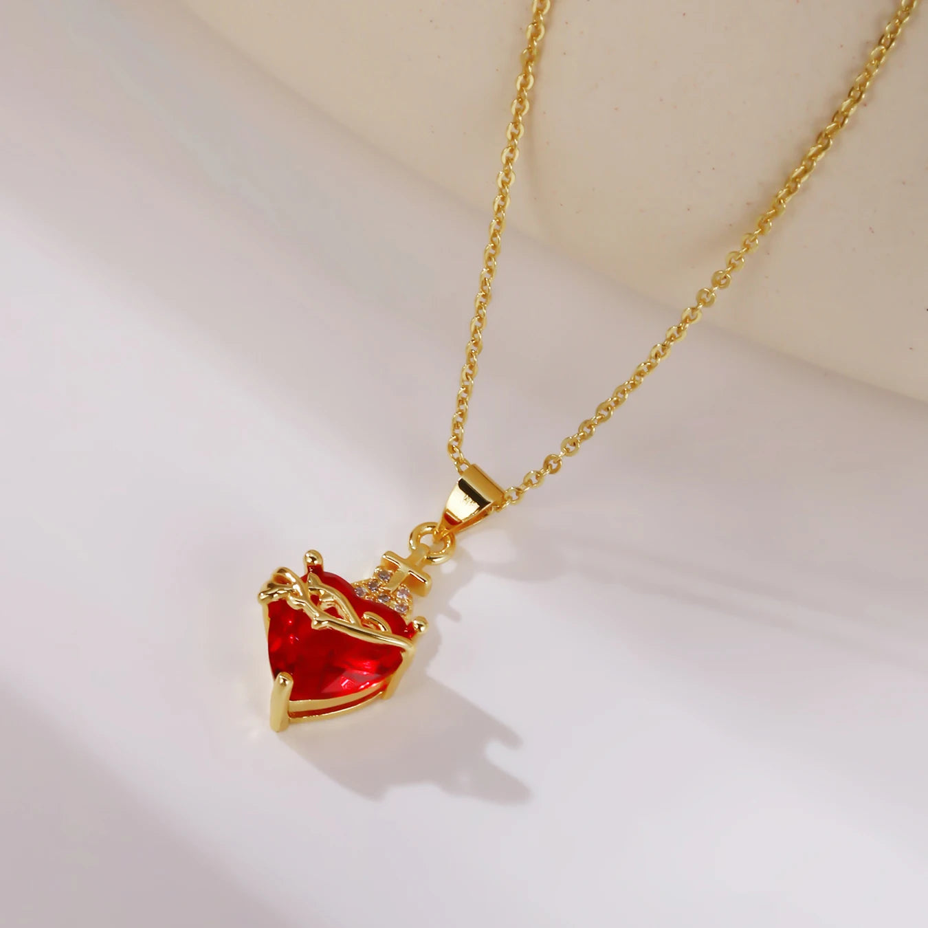 Gold necklace with a red heart-shaped pendant on a light background